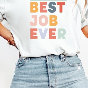 May include: A white t-shirt with the text "TEACHING KIDS ABOUT JESUS + BEST JOB EVER" in colorful block letters.