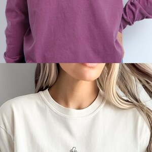 K&ouml;nnte beinhalten: Zwei Bilder eines wei&szlig;en T-Shirts mit einer Strichzeichnung einer Mutter und eines Kindes, die sich an den H&auml;nden halten. Der Text "In my full hands, full heart, era." ist auf das Shirt gedruckt.
