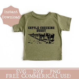 以下が含まれることがあります： 「Cattle Checking Buddy」という文字と、フェンスの後ろに牛の黒いシルエットが描かれた緑色のTシャツです。