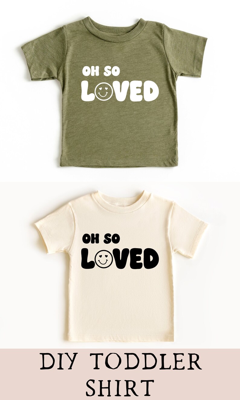 以下が含まれることがあります： 「Oh so loved」という文字と笑顔の顔が付いた幼児用Tシャツ2枚。Tシャツは色が異なり、1枚は緑色、もう1枚はクリーム色です。