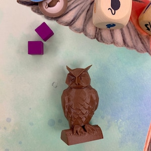 May include: A brown owl figurine with a geometric design, perched on a brown base. The owl has a detailed face with large eyes and a sharp beak.