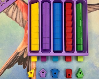 May include: A purple plastic tray with five compartments, each filled with wooden blocks in different colors: yellow, purple, blue, red, and green. Below the tray are five small birdhouses, each painted in a different color to match the blocks.