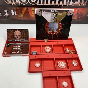 Peut inclure: Un organisateur rouge pour le jeu de société Gloomhaven, avec des compartiments pour les cartes et les jetons. Les cartes de jeu incluent une carte Giant Viper avec des statistiques et une icône de crâne. La boîte de jeu est visible en arrière-plan.
