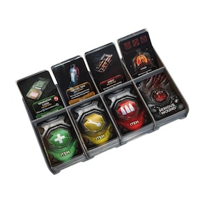 May include: A gray plastic game organizer filled with various game cards. The cards feature images and text such as "Termination Codes," "Oxygen Tank," "Ammo," "Lungs," and "Serious Wound." The cards are labeled "Item" and have icons like a plus sign, wrench, and bullets.