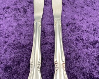 May include: Two silver dinner knives with ornate handles. The knives have a hammered finish and are on a purple background.