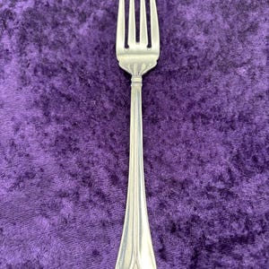 May include: A silver fork with a simple, elegant design. The fork has four tines and a long, slender handle.