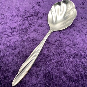 May include: A silver serving spoon with a decorative, scalloped bowl. The spoon has a twisted handle and is designed for serving desserts or sauces.