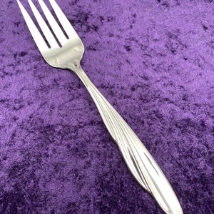 May include: A silver fork with a curved handle and a polished finish. The fork is lying on a purple velvet surface.