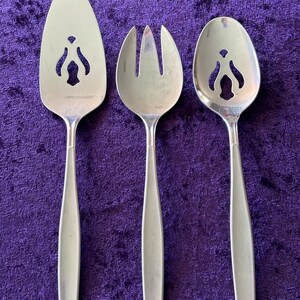 May include: Three silver serving utensils with decorative cutouts. The utensils include a serving spoon, a serving fork, and a cake server.