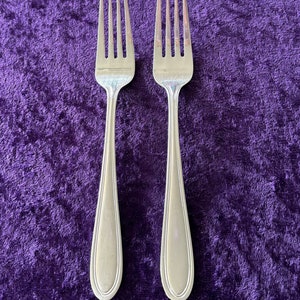 May include: Two silver forks with a polished finish, laid out on a purple velvet surface.