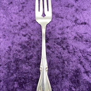 May include: A silver fork with a decorative handle. The fork has four tines and a pointed tip.