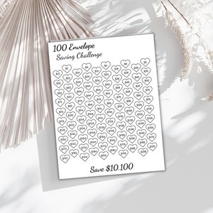 May include: A white paper with a black heart-shaped grid for a 100 Envelope Saving Challenge. The text "100 Envelope Saving Challenge" and "Save $10,100" are displayed. Each heart contains a different dollar amount.