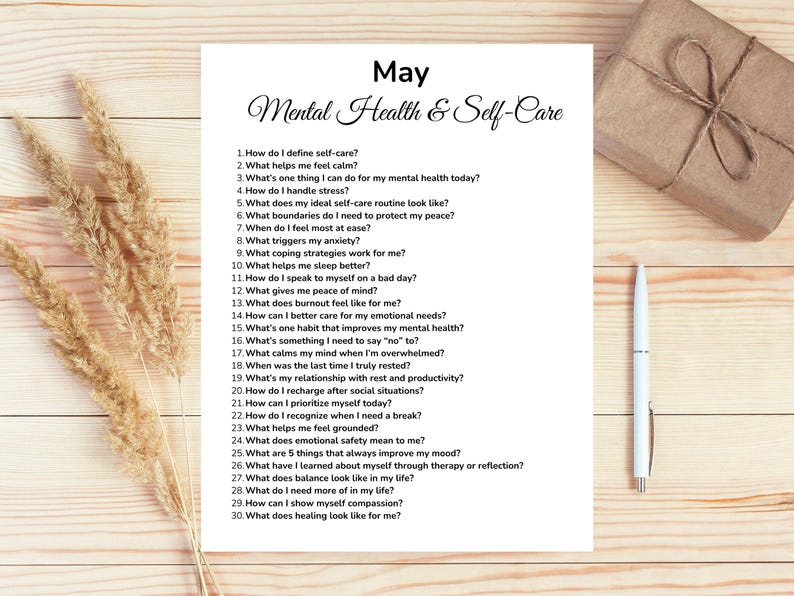 May include: A white sheet of paper with the title "May Mental Health & Self-Care" and a list of 30 self-reflection questions. A pen, a wrapped gift, and dried plants are also on the wooden surface.