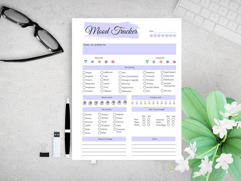 May include: A mood tracker sheet with a lavender header and sections for daily mood, feelings, stress, and energy levels. Includes checkboxes for activities and enough sleep, water, and food. A pen, glasses, and a keyboard are in the background.
