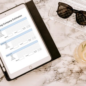 May include: A white tablet with a moving company estimates checklist. The checklist includes sections for company name, contact information, trucks, movers, and additional notes. The tablet is on a white marble surface with a glass of lemonade and sunglasses.