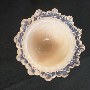 May include: A top-down view of a circular glass vessel featuring an opalescent finish. The rim is decorated with a series of rounded, bubble-like protrusions that create a scalloped edge. The interior of the glass is smooth and translucent.