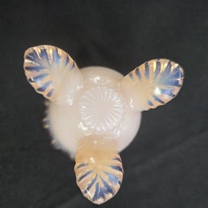May include: A pale, translucent opalescent glass bowl featuring three distinct feet with a ribbed, leaf-like pattern. The base of the bowl displays a central circular sunburst or starburst design, with the glass exhibiting a soft, milky white hue.