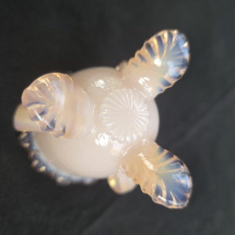 May include: A translucent opalescent glass bowl featuring a rounded base with a central sunburst pattern and three decorative feet. The glass exhibits a milky white appearance with subtle blue highlights along the edges and the textured feet.