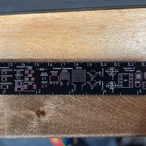 May include: A black ruler with white markings for measuring electronic components. The ruler includes common component sizes, such as SMD, MicroMELF, MiniMELF, SOT223, D2PAK, DIP, SSOP, QFP, and XTAL/OSC. The ruler is marked with inches and centimeters.