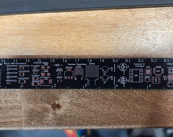 Könnte beinhalten: Ein schwarzes Lineal mit weißen Markierungen zum Messen von elektronischen Bauteilen. Das Lineal enthält gängige Bauteilgrößen wie SMD, MicroMELF, MiniMELF, SOT223, D2PAK, DIP, SSOP, QFP und XTAL/OSC. Das Lineal ist in Zoll und Zentimetern gekennzeichnet.