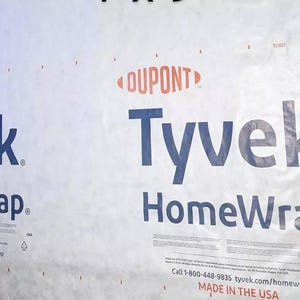 May include: A white Tyvek HomeWrap building wrap with the DuPont logo and the text "Tyvek HomeWrap" printed in blue. The text "Call 1-800-448-9835 tyvek.com/homewrap" and "Made in the USA" are also printed on the wrap.