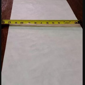 May include: A roll of white paper with a yellow measuring tape laid across it. The tape shows measurements in inches, with the paper extending beyond the 13-inch mark. The paper is on a dark brown surface.