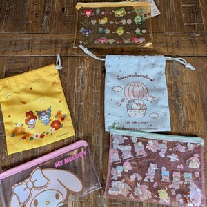 May include: An assortment of Sanrio character pouches and bags. The collection includes a yellow drawstring bag with floral and character designs, a pink zippered pouch with a My Melody graphic, and clear zippered pouches with various character illustrations.