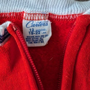 May include: Red Carter's brand zippered sleeper with white trim and a white tag that reads "Carter's 12 Months 19-22 LBS Machine Wash and Dry Warm Setting, No Wash Colors Separately Cool Iron If Needed".