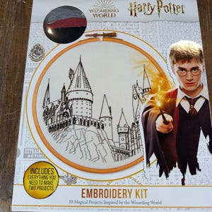 May include: A Harry Potter Wizarding World embroidery kit featuring a circular wooden hoop with a black line art illustration of a castle. The packaging includes a portrait of Harry Potter, embroidery thread, and text stating it includes everything needed to make two projects and 10 magical projects inspired by the Wizarding World.