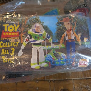 May include: A sealed plastic bag containing Disney's Toy Story toys from Burger King. The image shows Buzz Lightyear, Woody, and a small vehicle. Text on the packaging reads "TOY STORY NOW ON VIDEO COLLECT ALL 3 TOYS!"