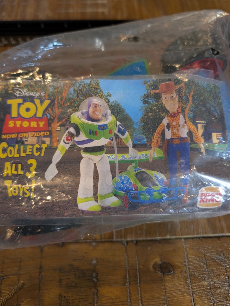 May include: A sealed plastic bag containing Disney's Toy Story toys from Burger King. The image shows Buzz Lightyear, Woody, and a small vehicle. Text on the packaging reads "TOY STORY NOW ON VIDEO COLLECT ALL 3 TOYS!"