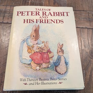 May include: A vintage copy of "Tales of Peter Rabbit and His Friends" by Beatrix Potter. The book cover features an illustration of several rabbits in colorful clothing. The title is in large, maroon letters, and the book is on a wooden surface.