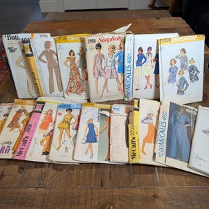 May include: A collection of vintage sewing patterns from brands including Simplicity, McCall's, and Butterick. The paper envelopes feature illustrations of various clothing styles, including dresses, suits, and tops, with printed text indicating pattern numbers.