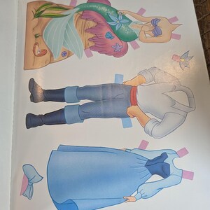 May include: A page from a children's paper doll book featuring three cut-out figures. The figures include a mermaid with a teal tail, a man in blue pants and a white shirt, and a woman in a blue dress. The figures have tabs for easy assembly.