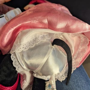 Peut inclure: Une poup&eacute;e en peluche de Minnie Mouse, vue de dos, avec une robe en satin rose et un jupon blanc bord&eacute; de dentelle. La poup&eacute;e a une queue noire et une &eacute;tiquette "Disneyplan".