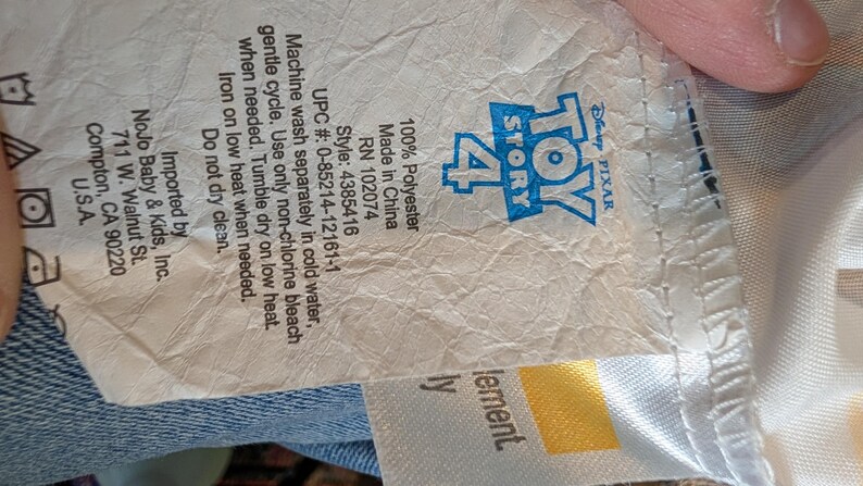 May include: A white fabric care label for a Toy Story 4 product. The label features the blue Toy Story 4 logo, 100% Polyester material content, style number 4385416, UPC 0-85214-12161-1, and care instructions including machine wash cold and tumble dry low.