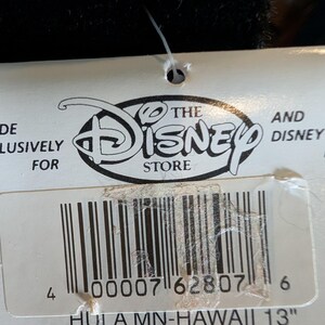 May include: A white tag with the Disney Store logo and barcode. Text on the tag reads "HULA MN-HAWAII 13". The tag is attached to a black object. The tag is approximately 13 inches in length.