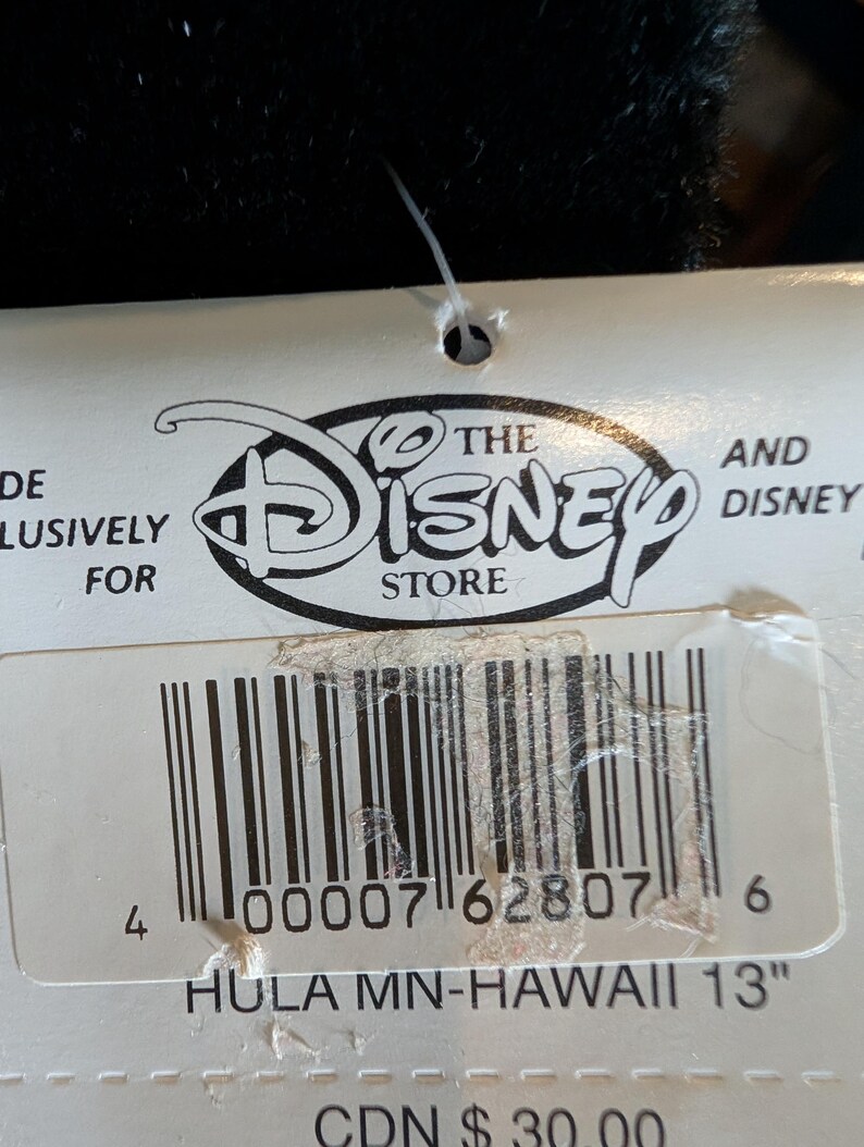 May include: A white tag with the Disney Store logo and barcode. Text on the tag reads "HULA MN-HAWAII 13". The tag is attached to a black object. The tag is approximately 13 inches in length.