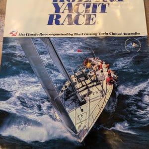 May include: A vintage poster for the 41st AWA Sydney Hobart Yacht Race, featuring a sailboat cutting through choppy waves. The poster is white with blue and red text, and the race start date is December 26th, 1985.