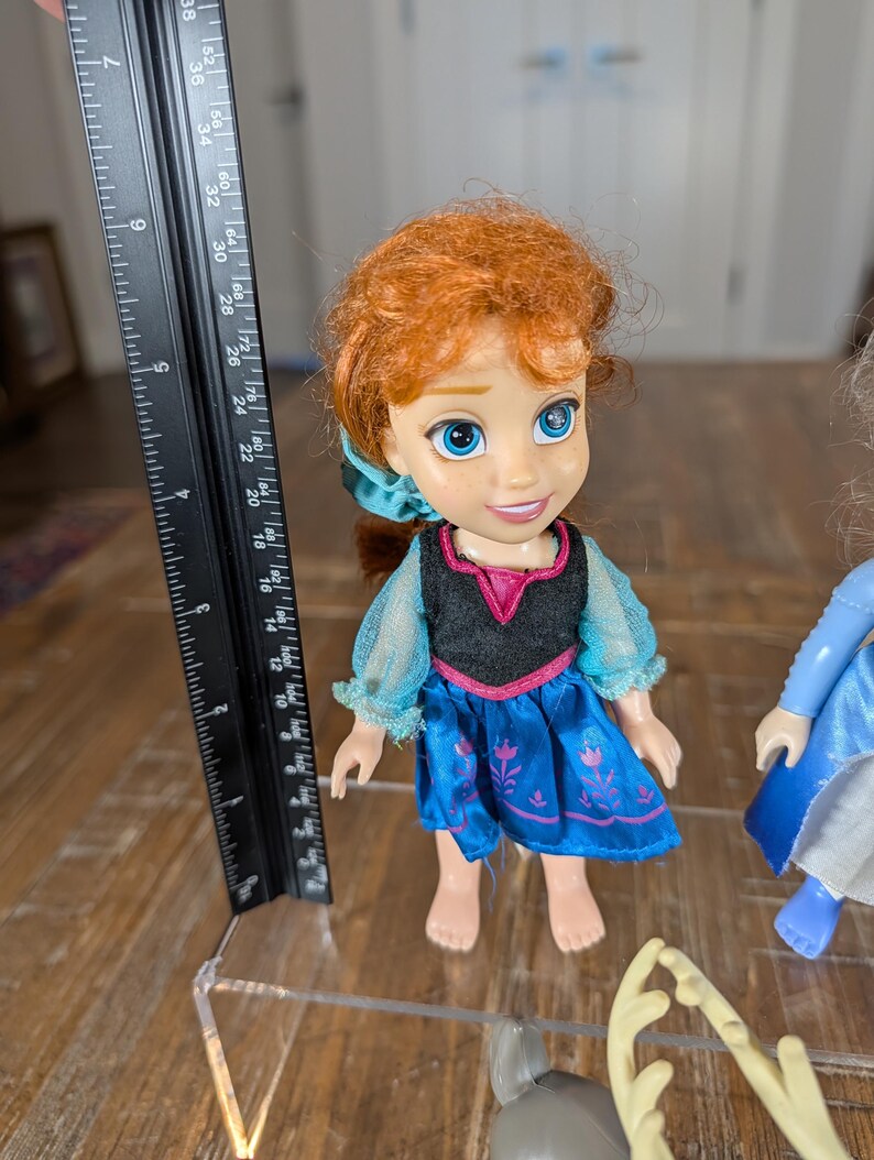 May include: A doll of a character with red hair, wearing a blue dress with a black bodice and a pink neckline. The doll is approximately 5 inches tall. A ruler is next to the doll.