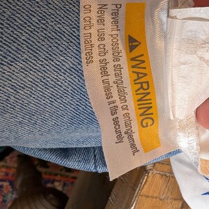 May include: A light blue fabric item featuring a white care label with a yellow warning banner. The text reads: WARNING Prevent possible strangulation or entanglement. Never use crib sheet unless it fits securely. A white fabric with blue stars.