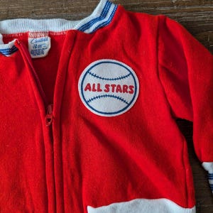 May include: Red and white baseball jacket with blue stripes and a white patch with a baseball and the text "ALL STARS" on the front.