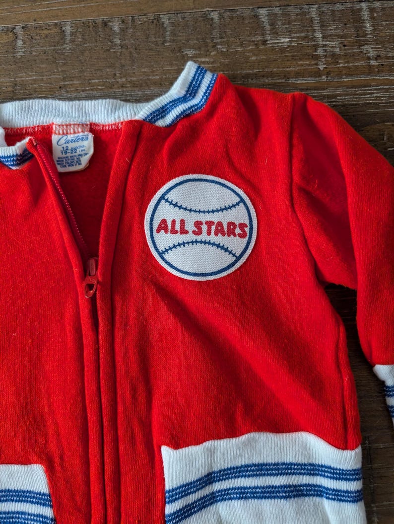 May include: Red and white baseball jacket with blue stripes and a white patch with a baseball and the text "ALL STARS" on the front.