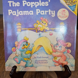 May include: A vintage children's book titled "The Popples' Pajama Party" with colorful illustrations of cartoon characters. The cover features the title in large, playful letters and images of the characters in a bedroom setting.