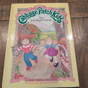 May include: A vintage Cabbage Patch Kids storybook titled "The Just-Right Family." The cover features illustrations of two Cabbage Patch Kids holding hands, with a fox and a forest scene in the background. The book is a Parker Brothers Story Book.