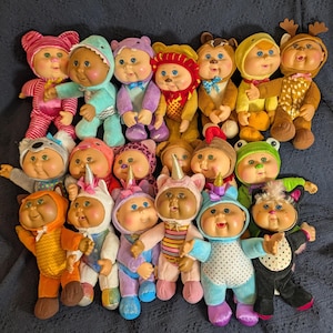 May include: A collection of twenty Cabbage Patch Kids dolls arranged in rows, each wearing a unique plush animal or creature costume, including various colors like pink, blue, purple, orange, and brown, with soft vinyl faces and yarn hair.