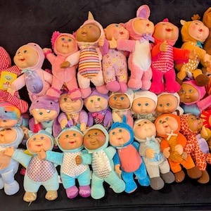 May include: A white ceramic mug with a black handle and the text "But First, Coffee" in a bold, black font. The mug is filled with a dark liquid, likely coffee, and sits on a light-colored surface.