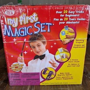 May include: A red and yellow box for a My First Magic Set containing over 20 easy tricks for beginners. The packaging features a child in a white shirt and black bowtie holding a magic wand, with illustrations of vanishing crayons and magic tricks.