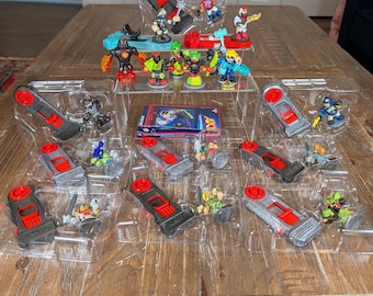 May include: A collection of Akedo action figures and their corresponding battle controllers, featuring various characters with distinct colors and weapons, arranged in clear plastic packaging on a tiered display stand with a small instruction booklet.