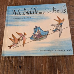 May include: A vintage children's book titled "Mr. Biddle and the Birds" by Lonzo Anderson, illustrated by Adrienne Adams. The cover features a whimsical illustration of a person in a blue carriage pulled by birds against a blue sky.